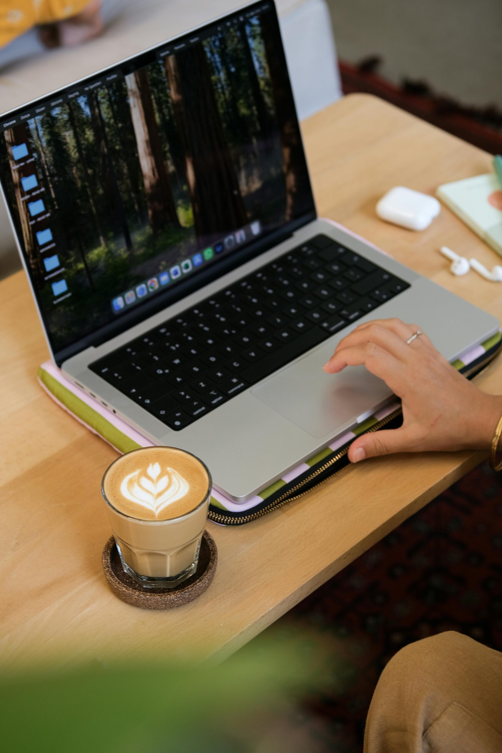 A cozy workspace with a laptop, latte, and wireless earbuds, exuding productivity and comfort.