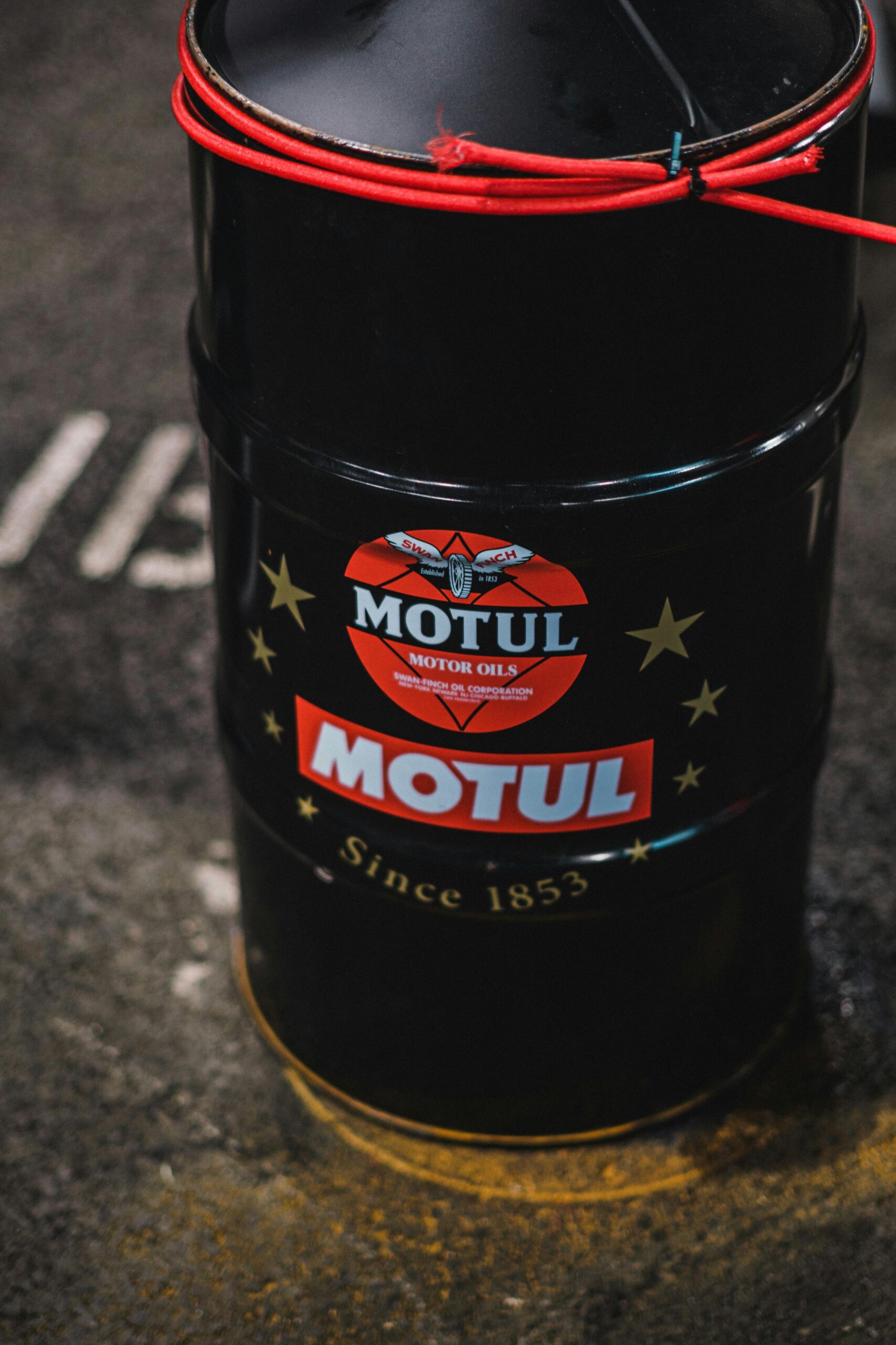 High angle view of Motul oil barrel with logo and text on a garage floor.